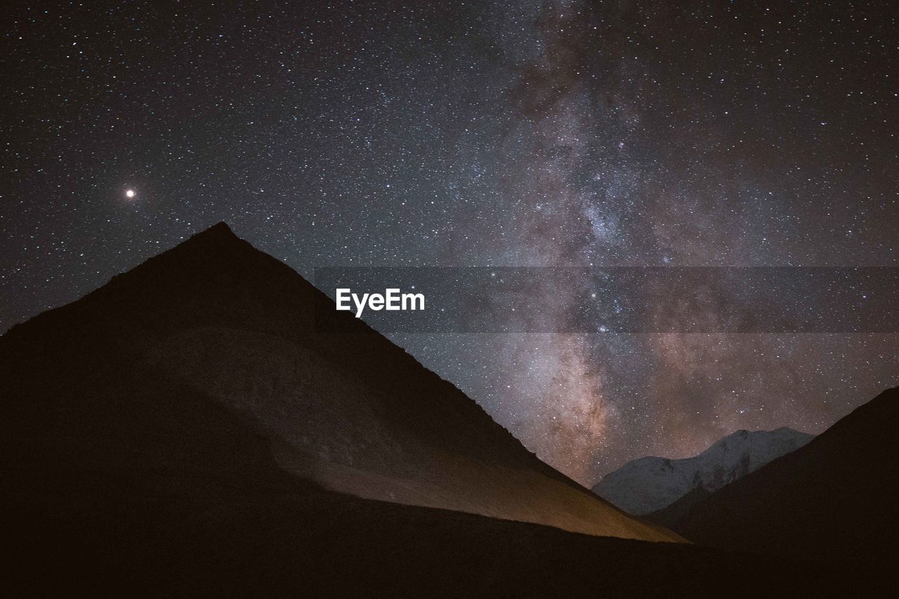 LOW ANGLE VIEW OF MOUNTAIN AGAINST STAR FIELD