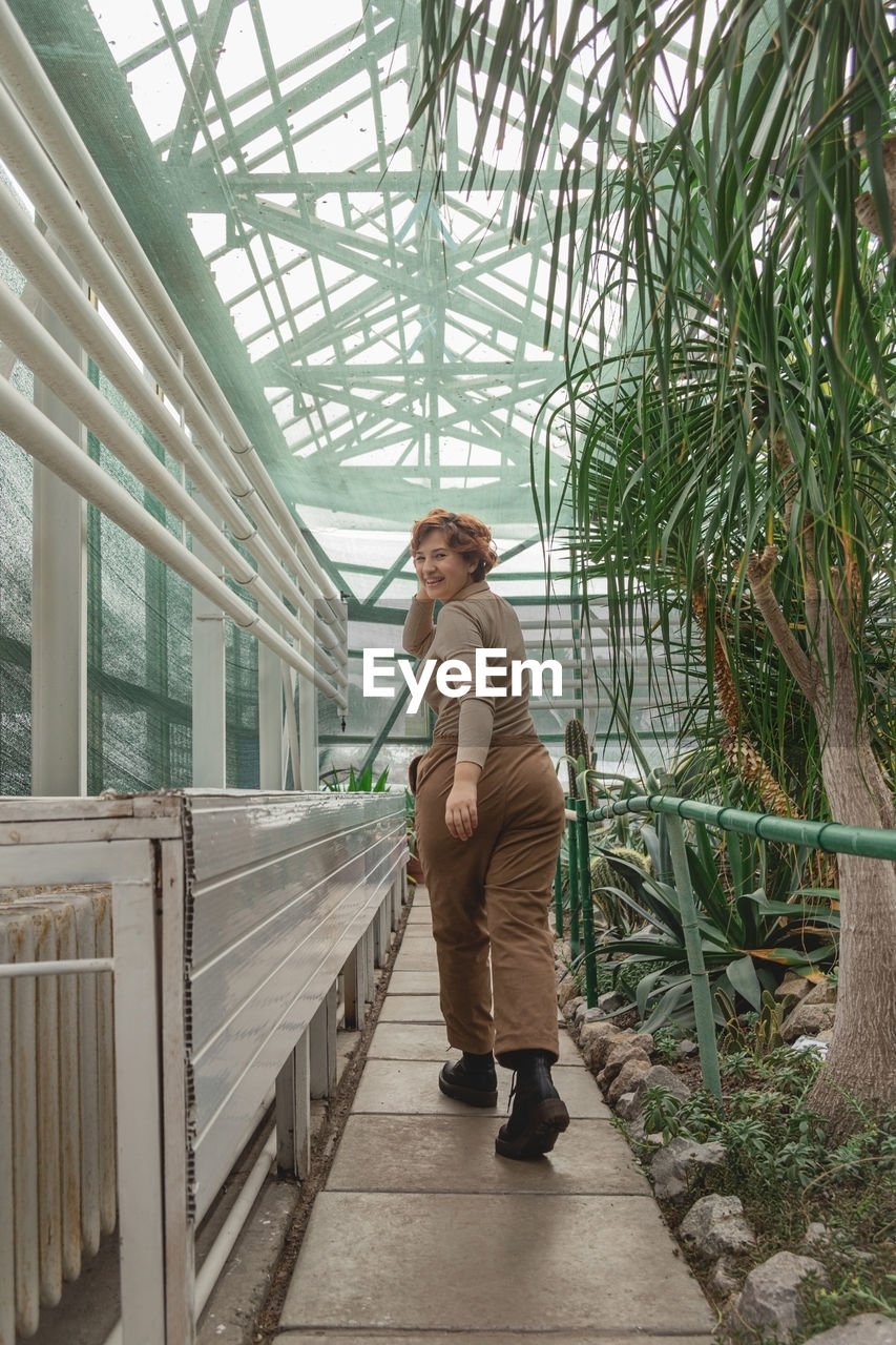 A beautiful plus size girl runs across greenhouse among the green plants. cottagecore style.