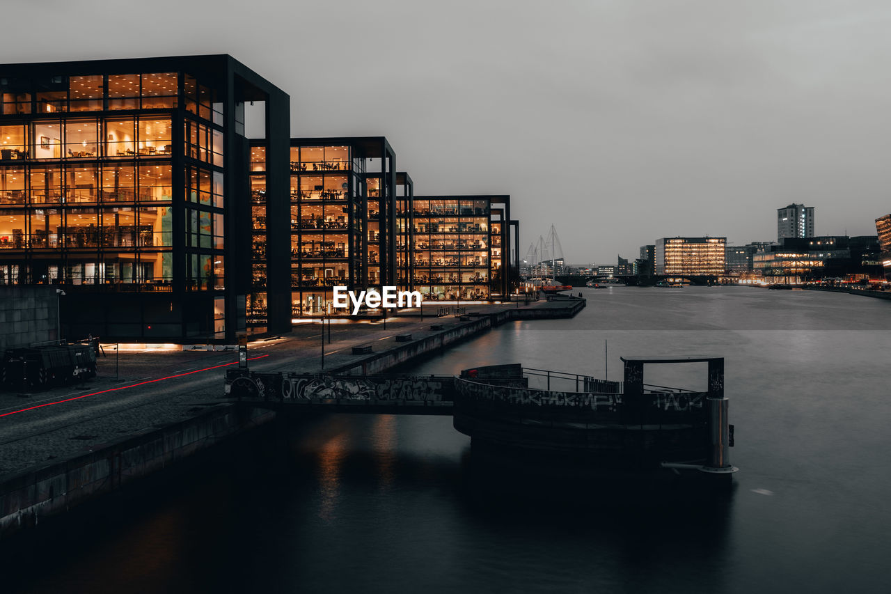 Buildings by river against sky at dusk