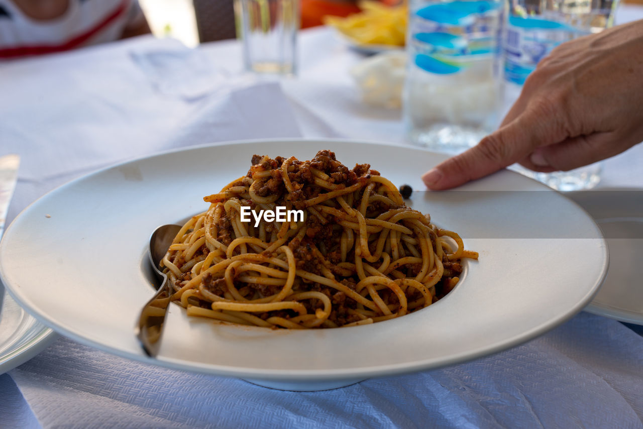 Plate full of spaghetti bolognese. finger pointing at food.