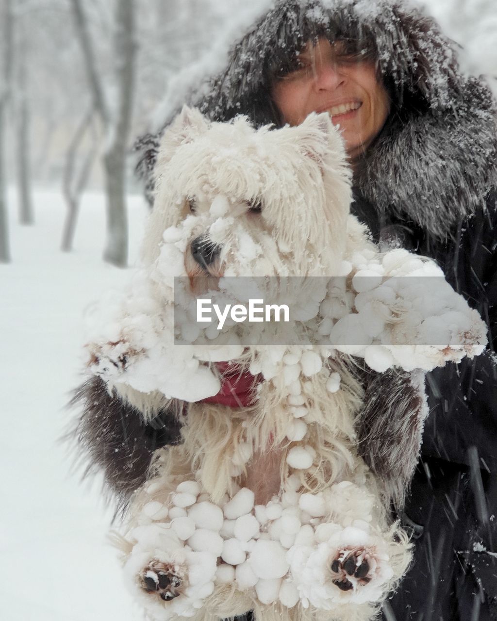 Smiling woman with dog standing outdoors during snowfall