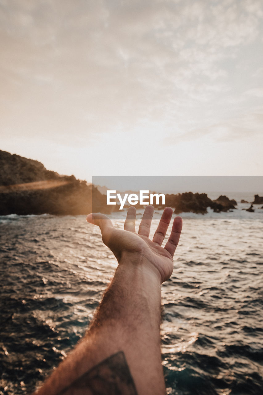 Person hand by sea against sky