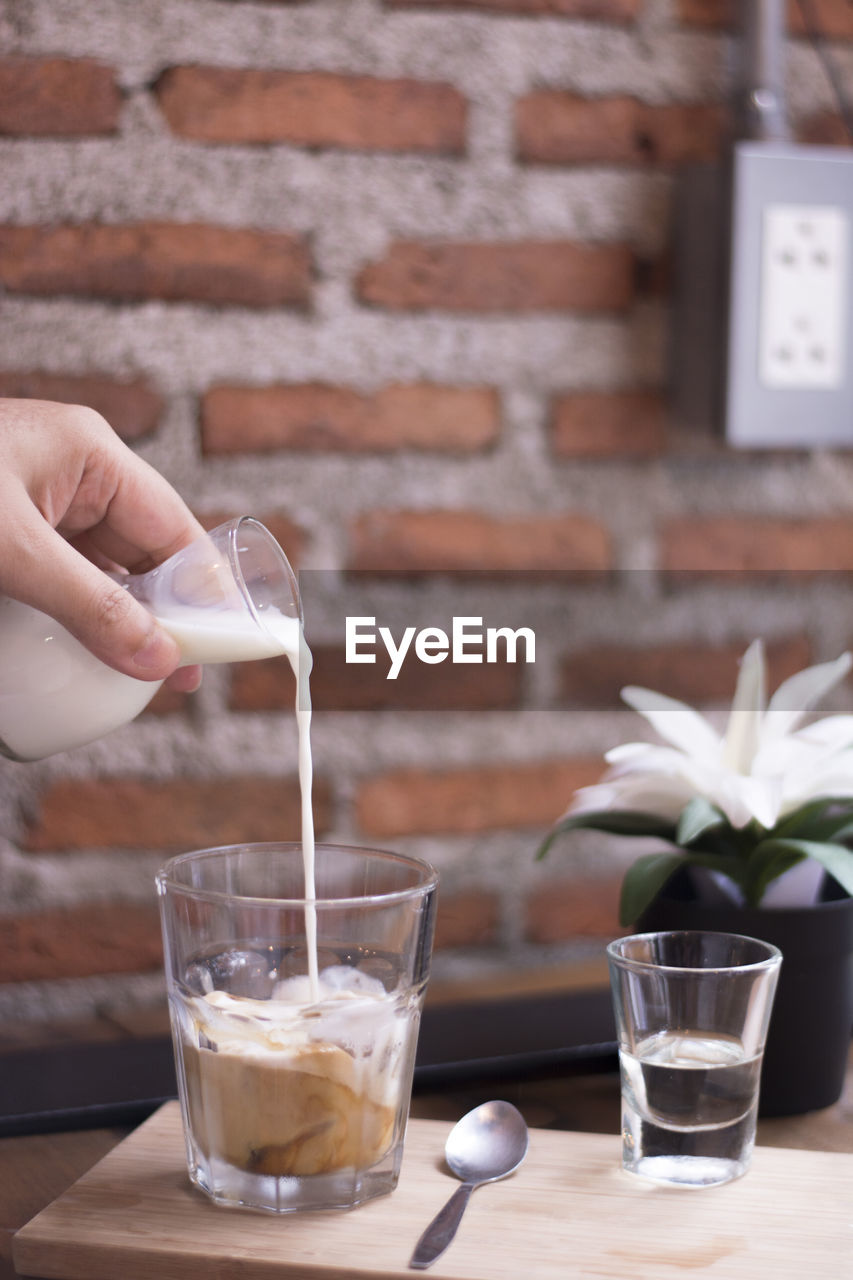 Cropped hand of person pouring milk in coffee on table