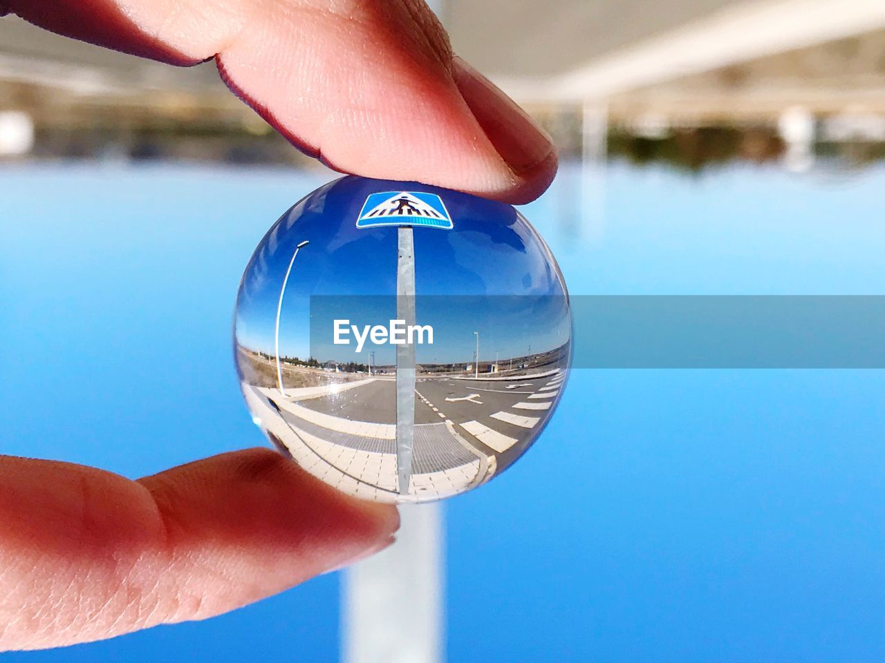 Close-up of hand holding crystal ball against blue sky