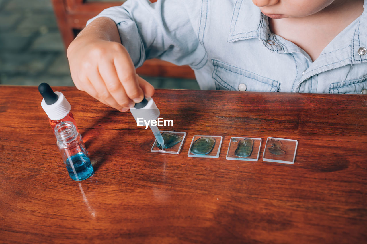 Little boy laboratory activity with colored water, pipette and pieces of glass.