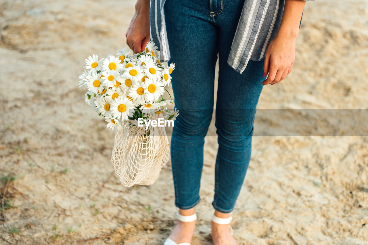 Low section of woman holding flowers while standing on rock