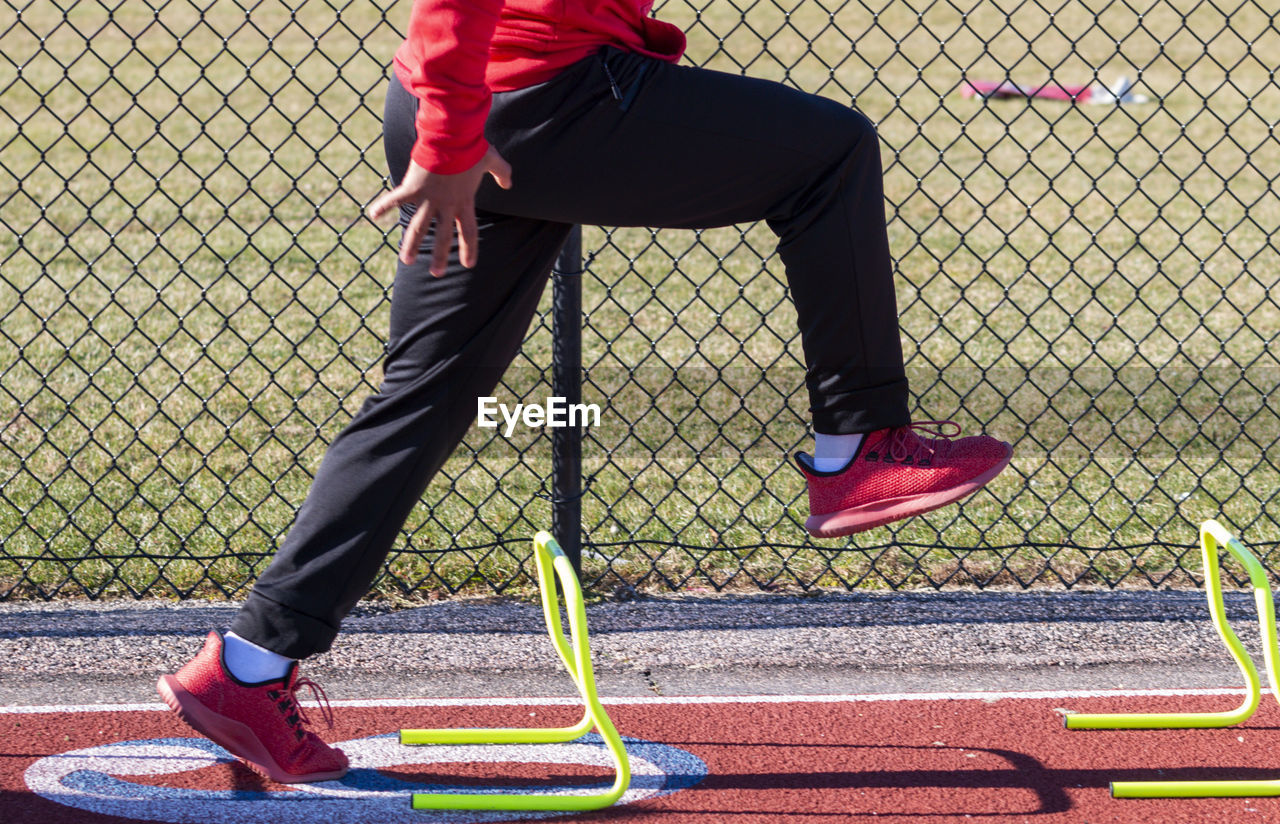 Track runner standing over yellow mini hurdles in the a-position preforming speed training drills.