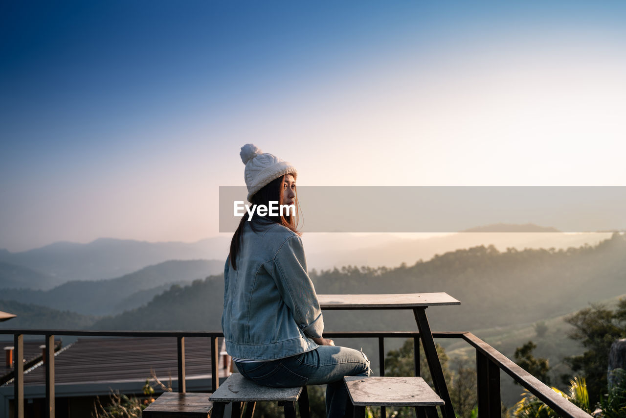 Woman sitting on stool in balcony against mountain during winter