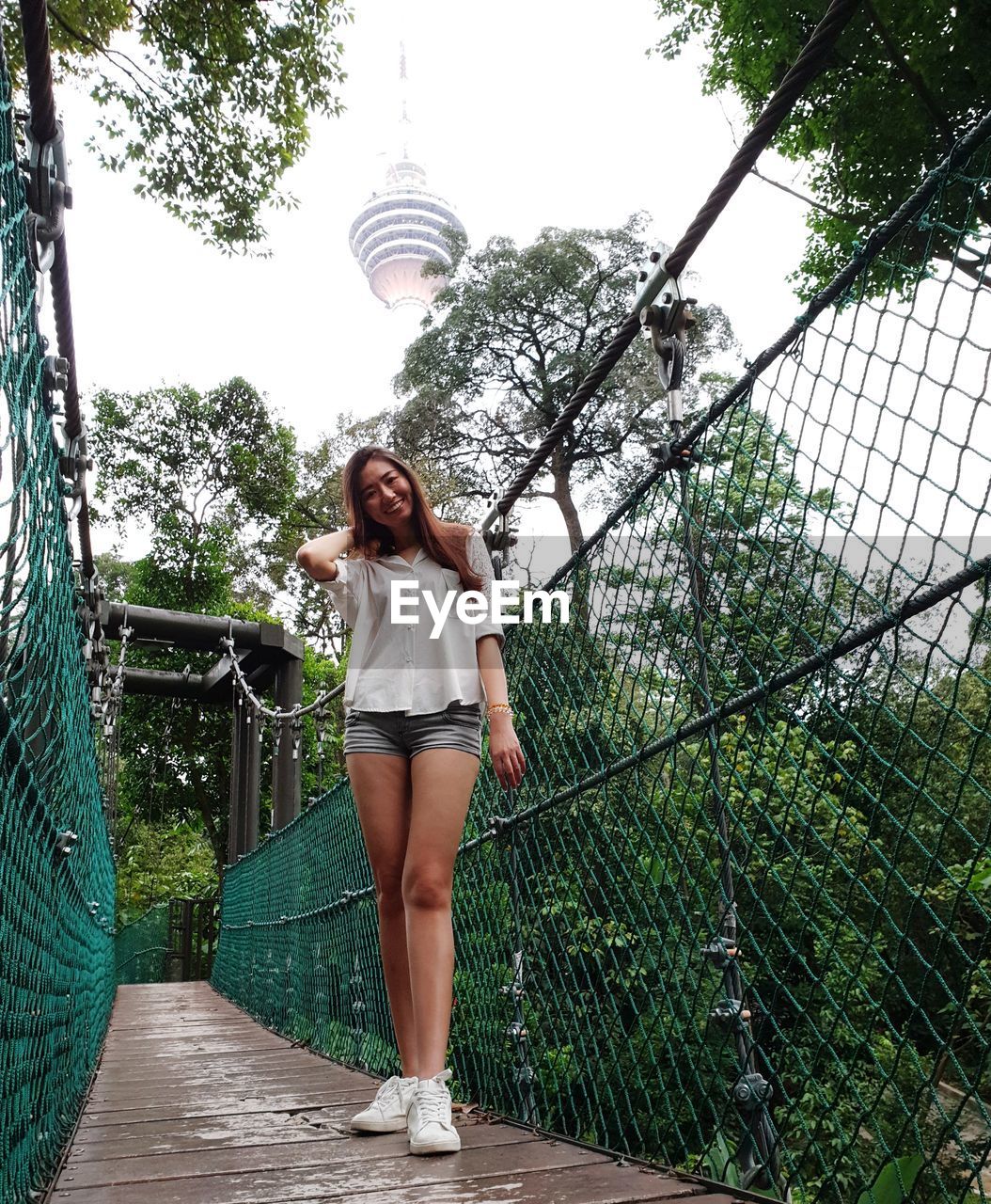 FULL LENGTH PORTRAIT OF YOUNG WOMAN STANDING AGAINST TREES