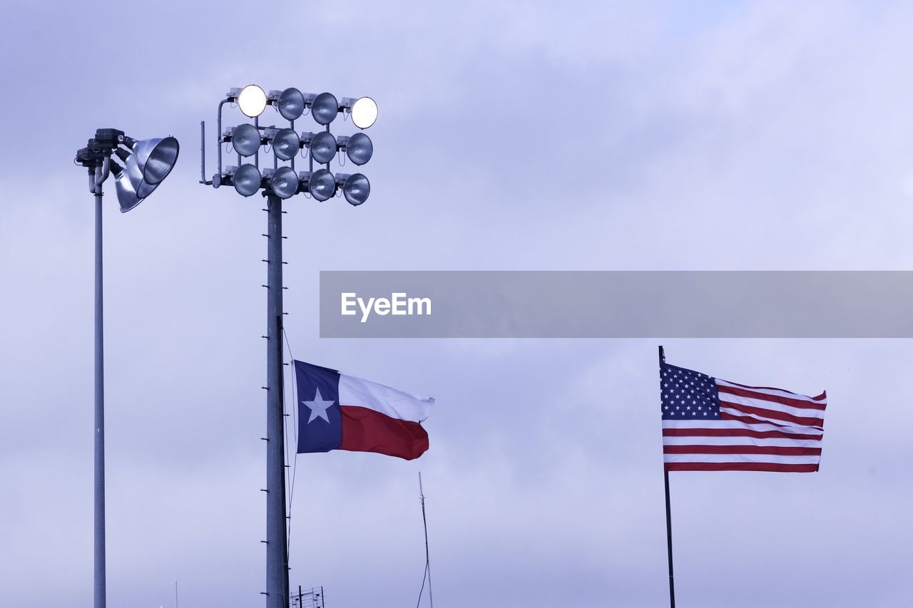 Low angle view of floodlights and flags against sky