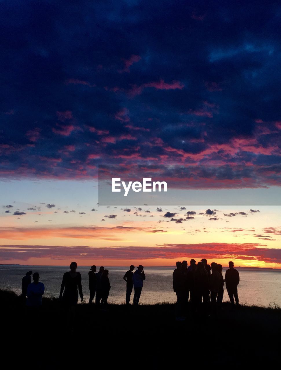 Silhouette people standing by sea during sunset