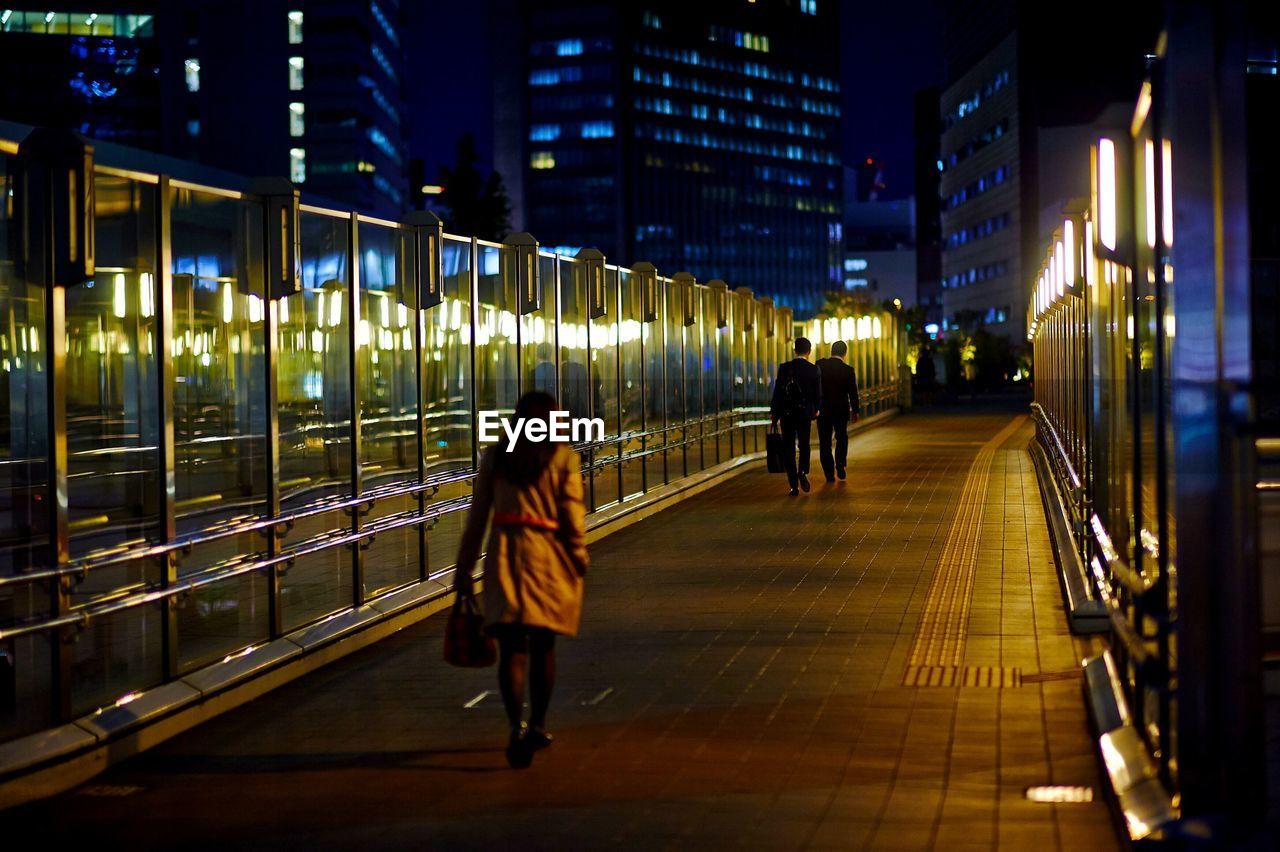 Rear view of people walking on elevated walkway at night