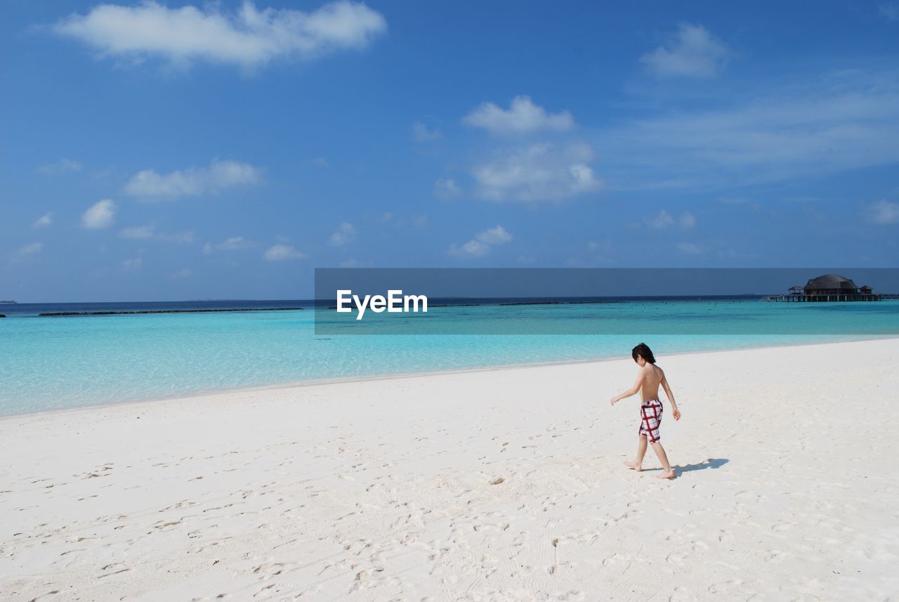 Full length of shirtless boy walking on beach against sky