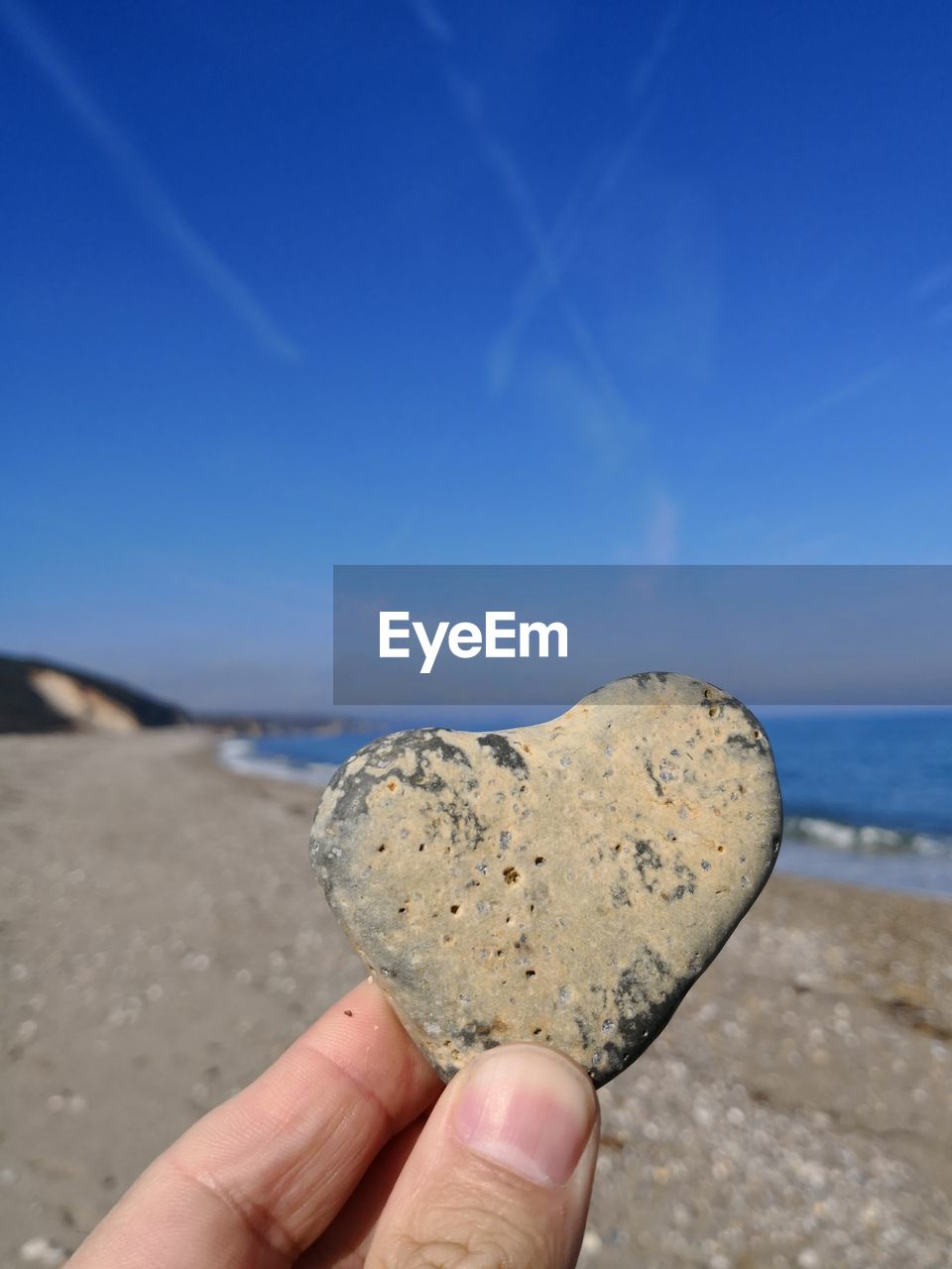 Cropped hand holding heart shape rock at beach against sky