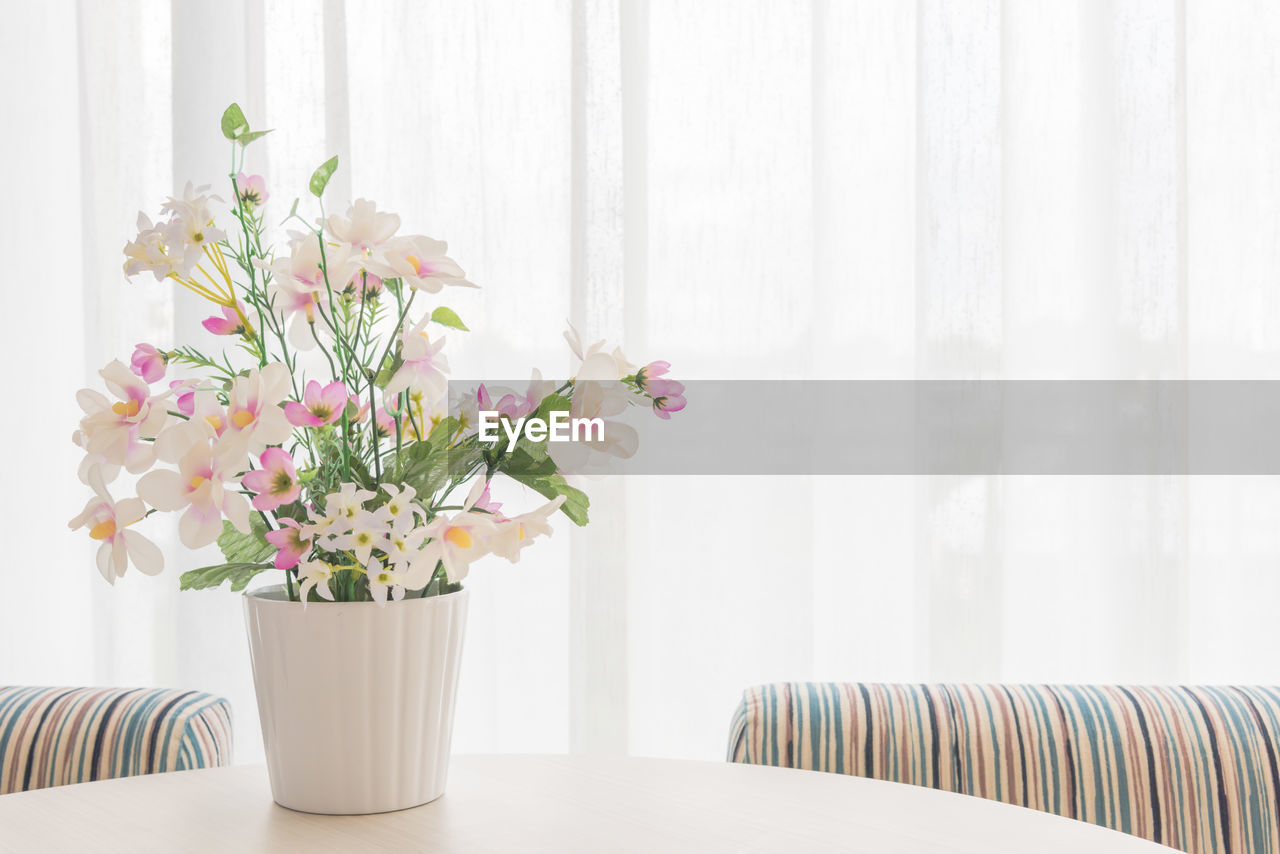 Flower vase on table against window at home