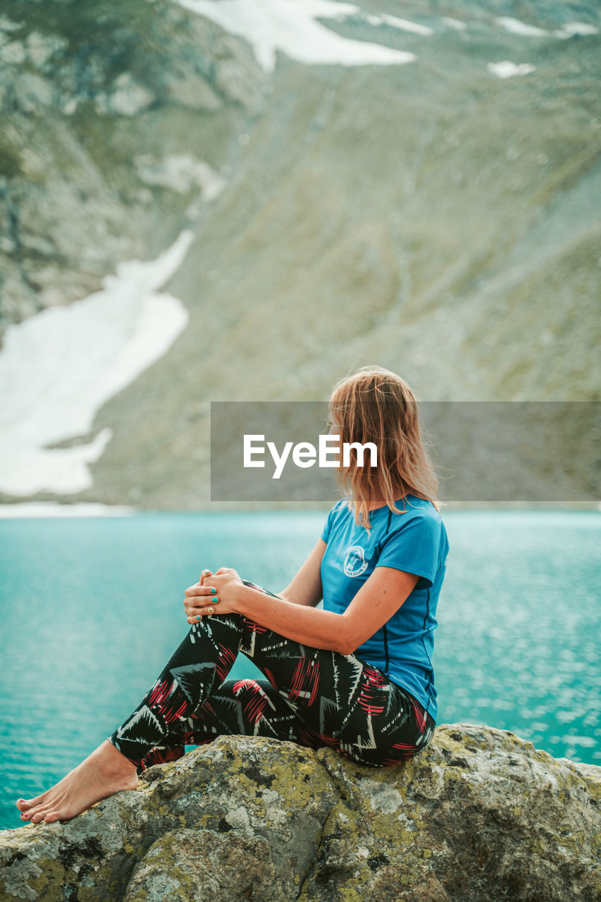 WOMAN SITTING ON ROCK AGAINST SEA