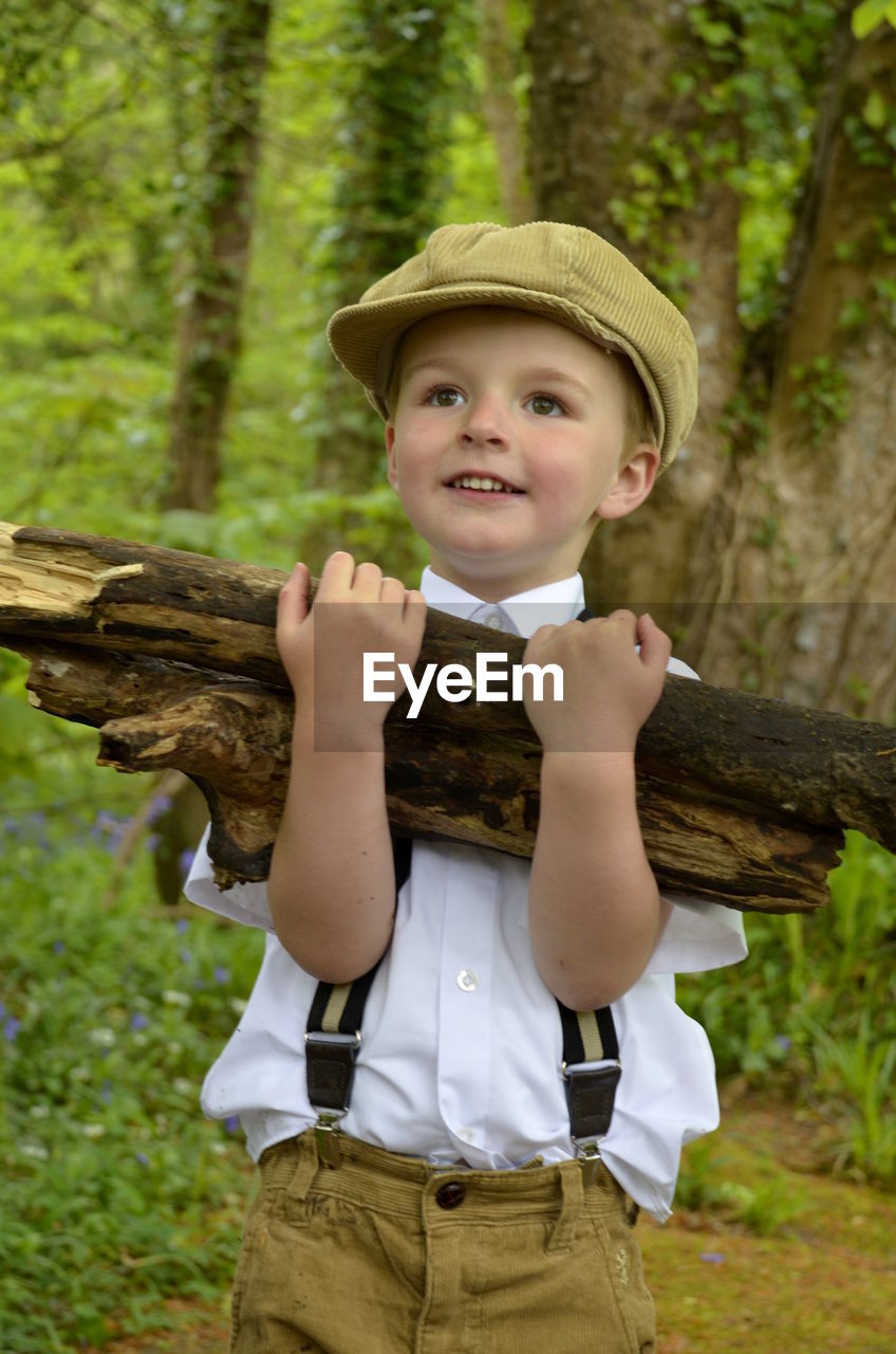 Low angle view of cute boy holding firewood while standing in forest