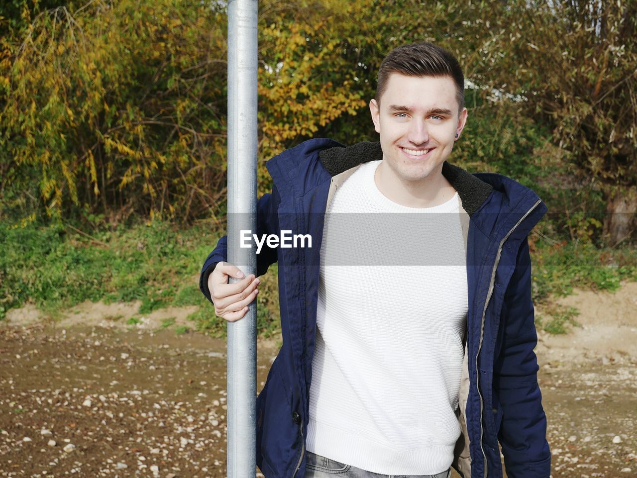 Portrait of smiling young man standing by pole against plants
