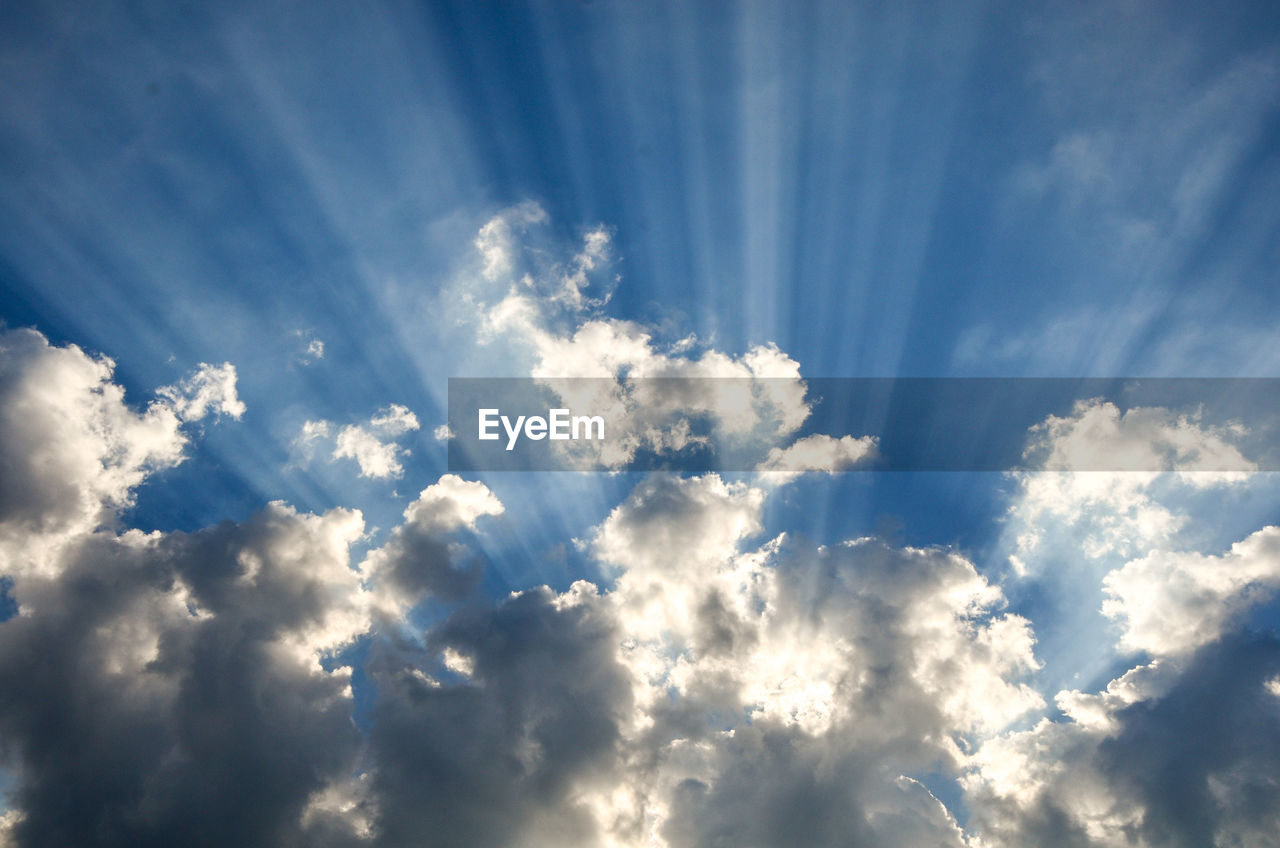 Low angle view of sunlight streaming through clouds