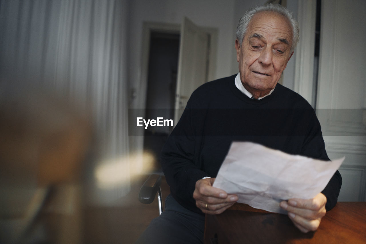 Senior man sitting at table at home reading a paper