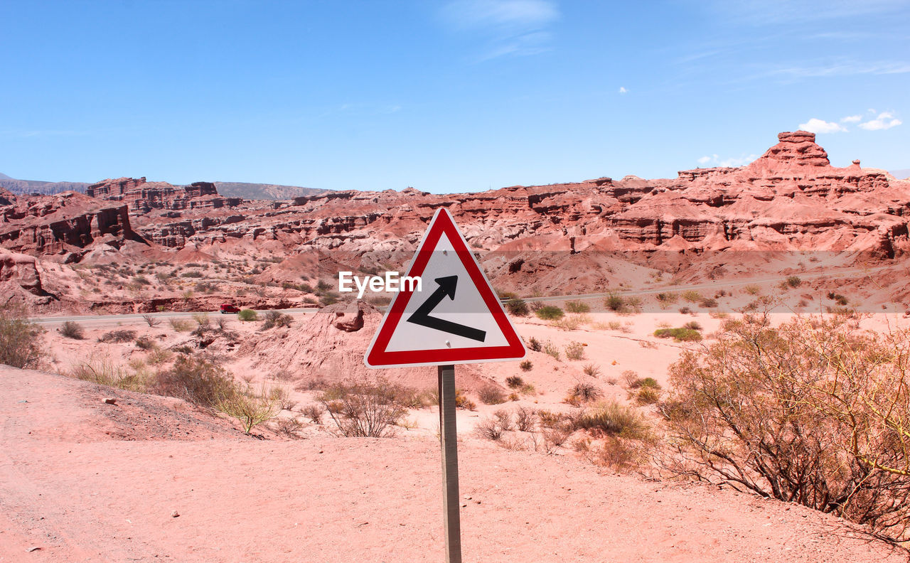 Road sign in desert against sky