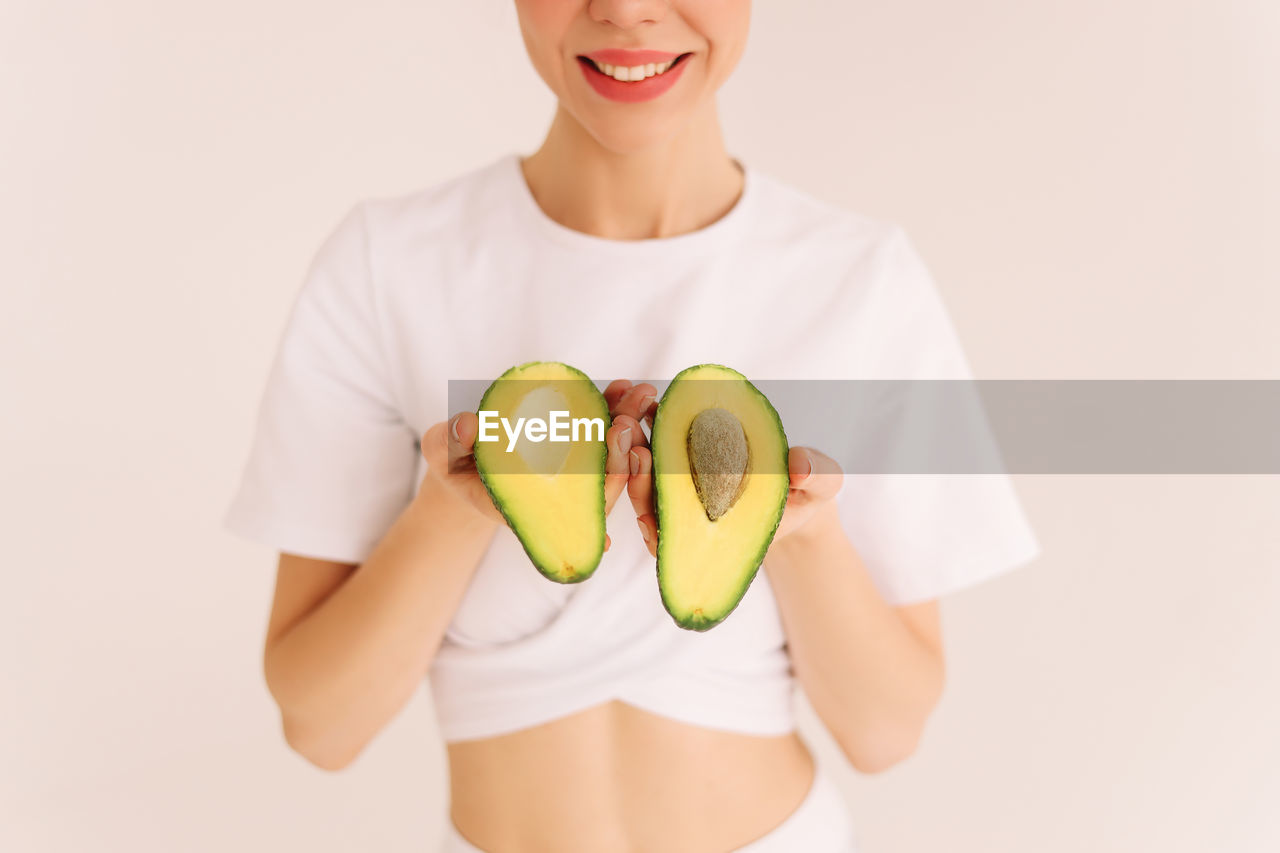 Smiling healthy young woman holds vegetables fruits green avocado on a white isolated background