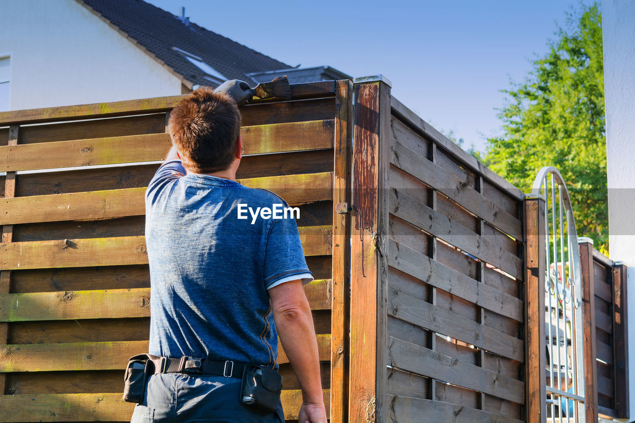 Rear view of man painting wooden fence
