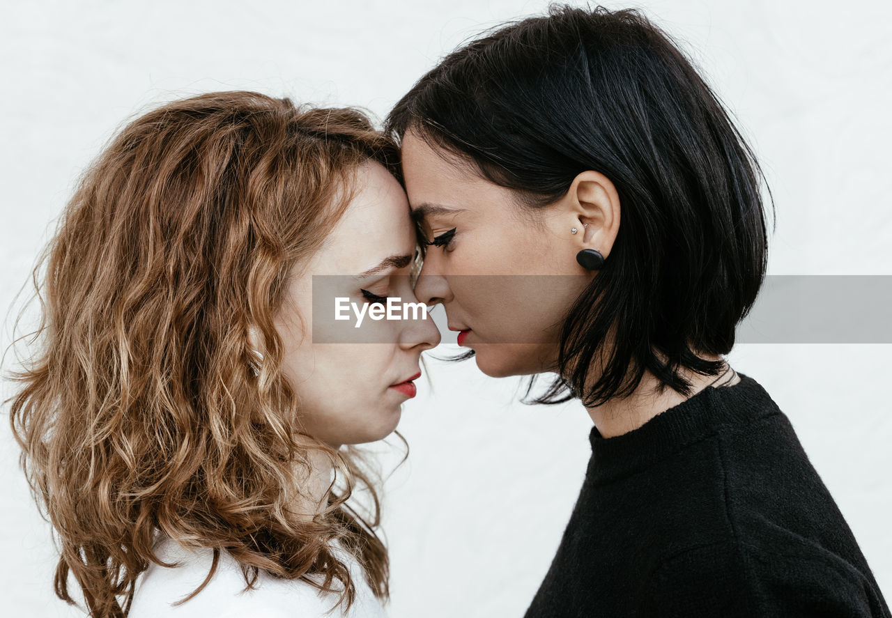 Side view of lesbian couple with eyes closed standing face to face against wall