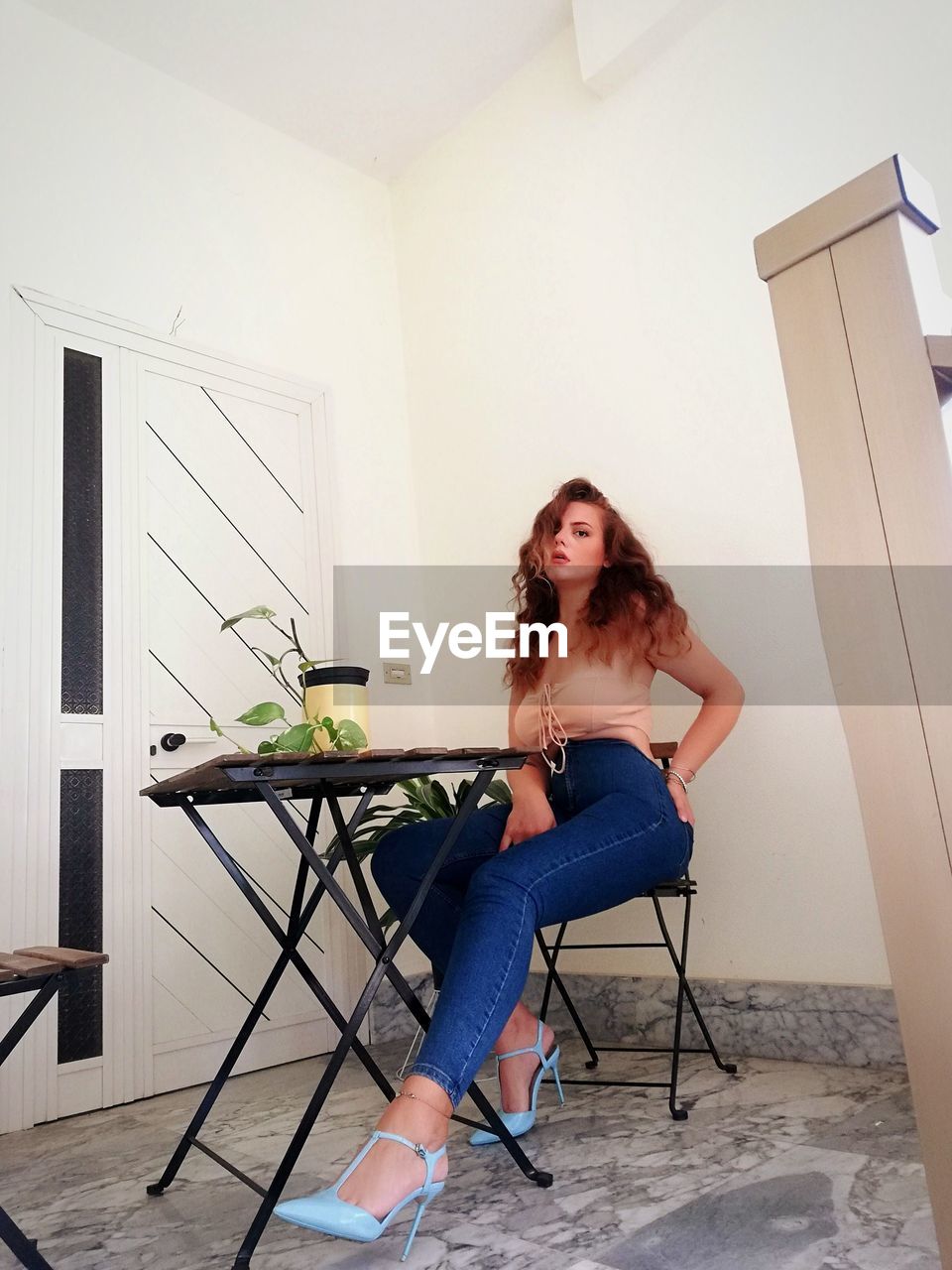 FULL LENGTH PORTRAIT OF YOUNG WOMAN SITTING ON CHAIR AT HOME