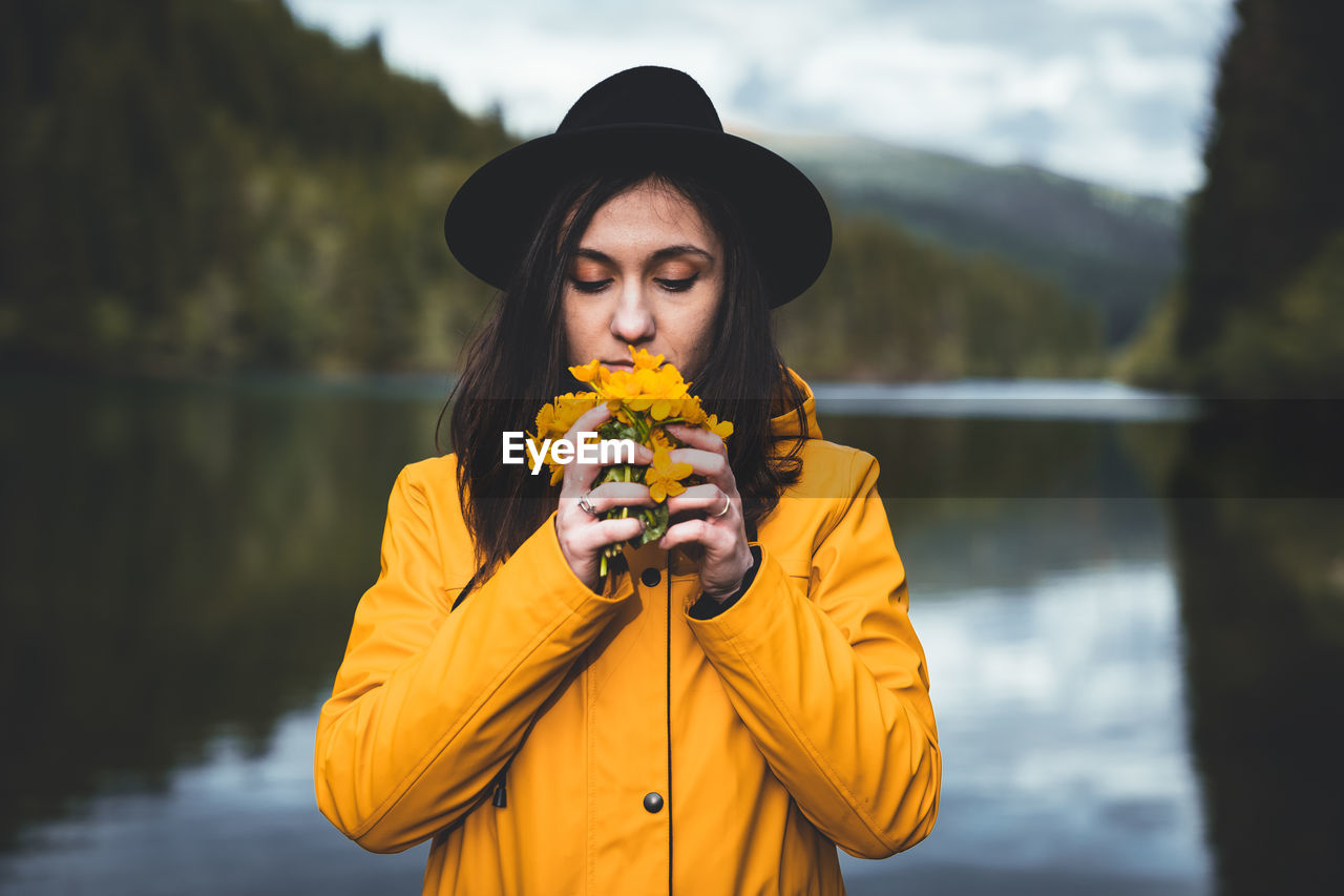 Young woman holding yellow flowers while standing by lake