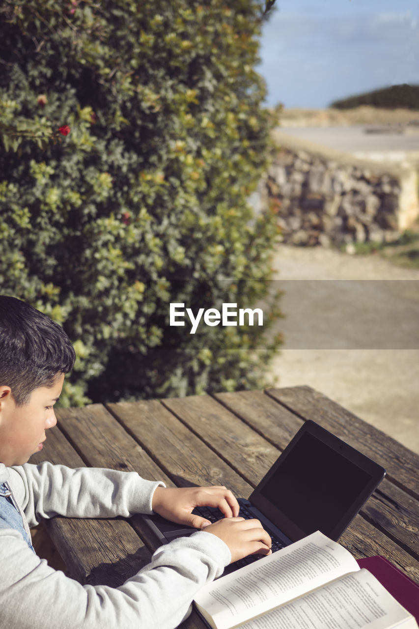 Young latin student, outdoors, using laptop sitting at a park