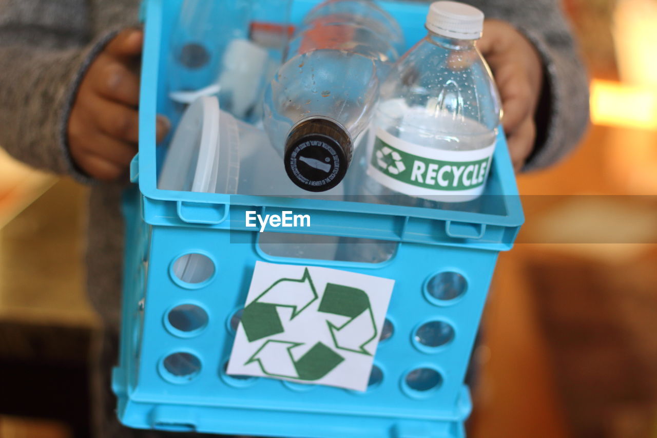 Midsection of person holding basket with plastic bottles