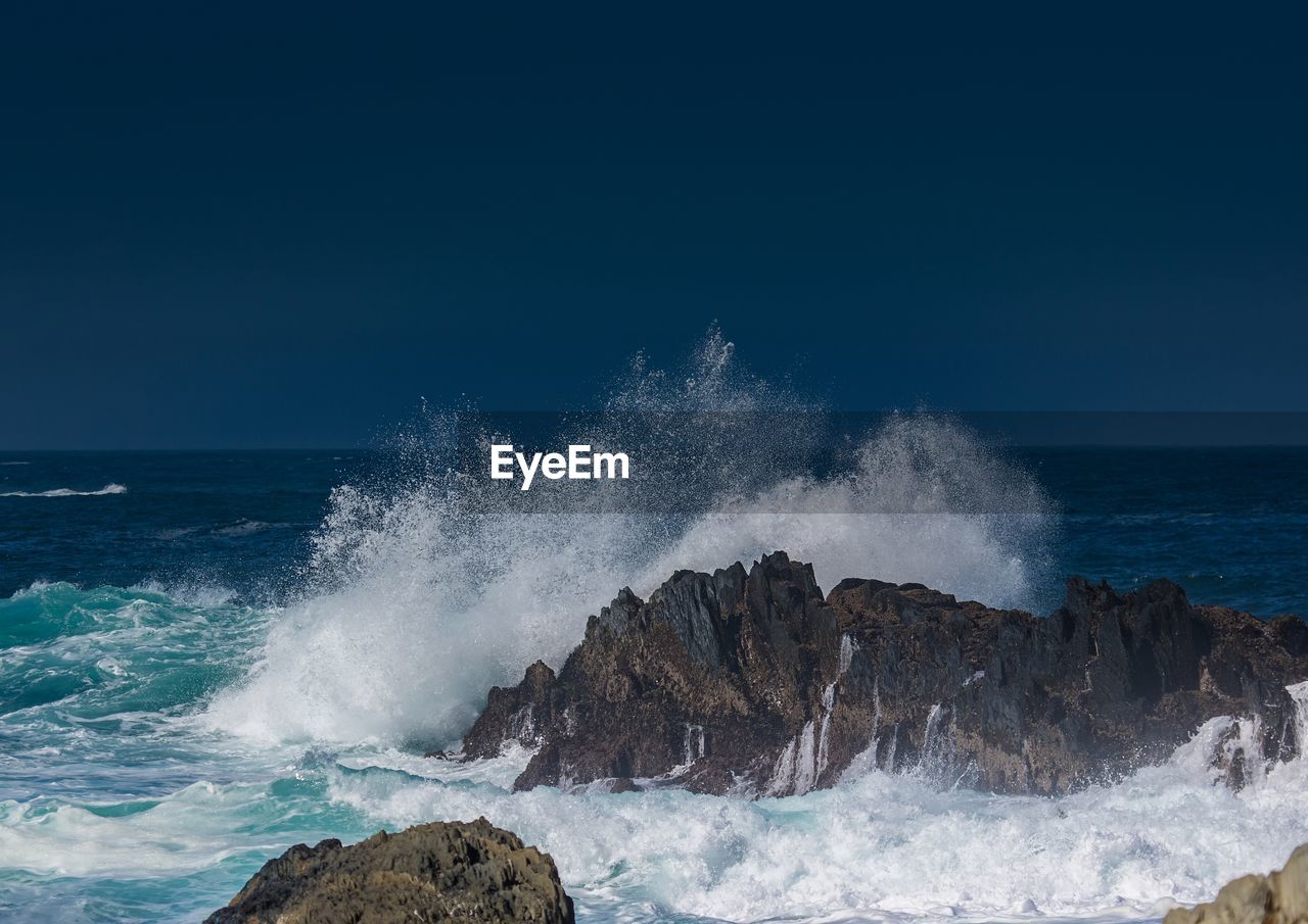 WAVES SPLASHING ON ROCKS AGAINST SKY