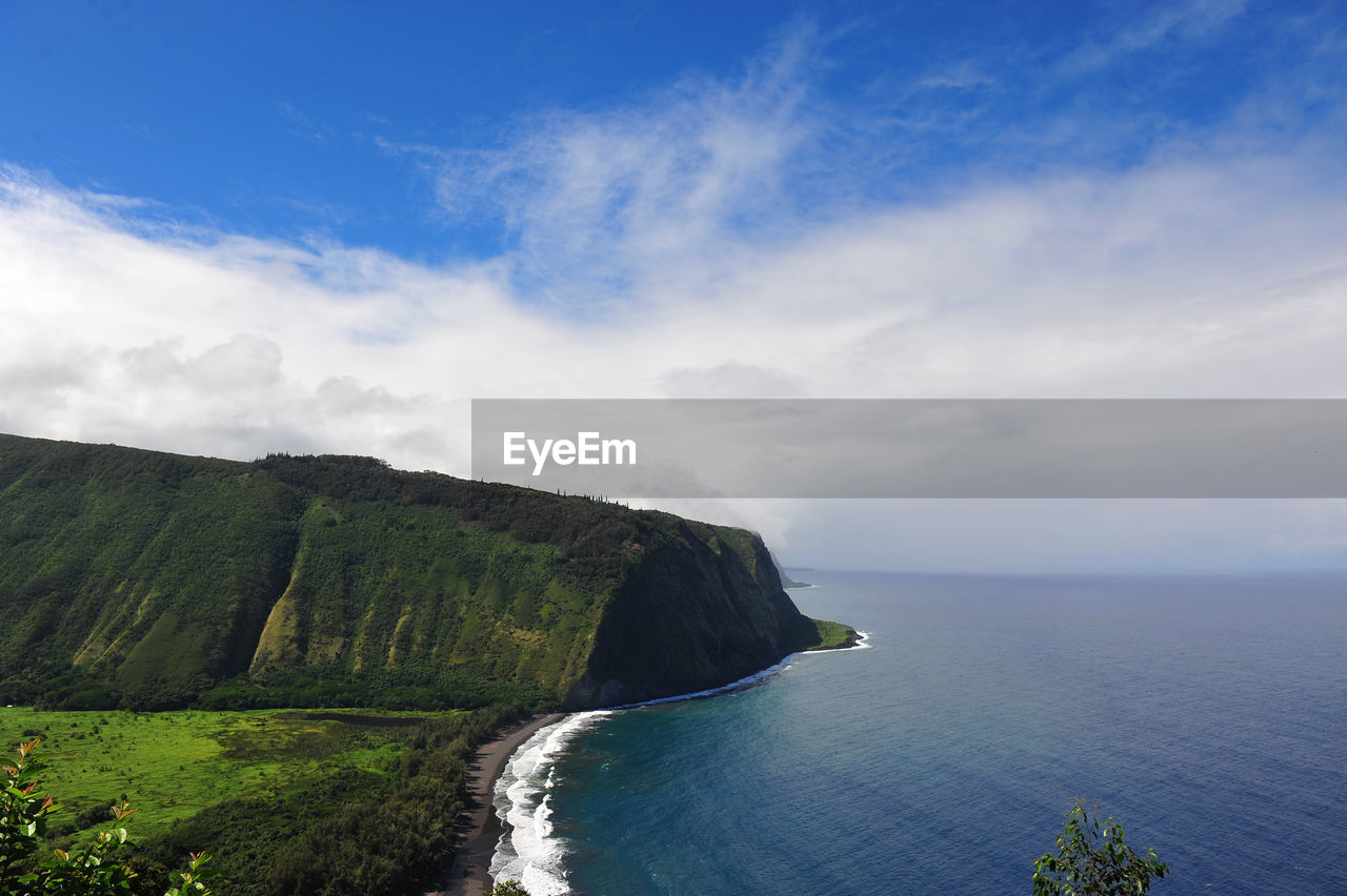 Scenic view of sea by mountain against cloudy sky