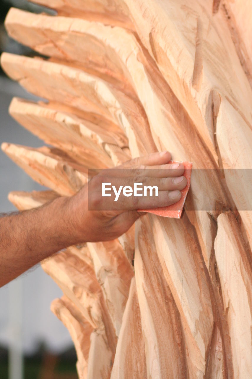 Cropped image of artist smoothing surface of wood sculpture with sandpaper in workshop