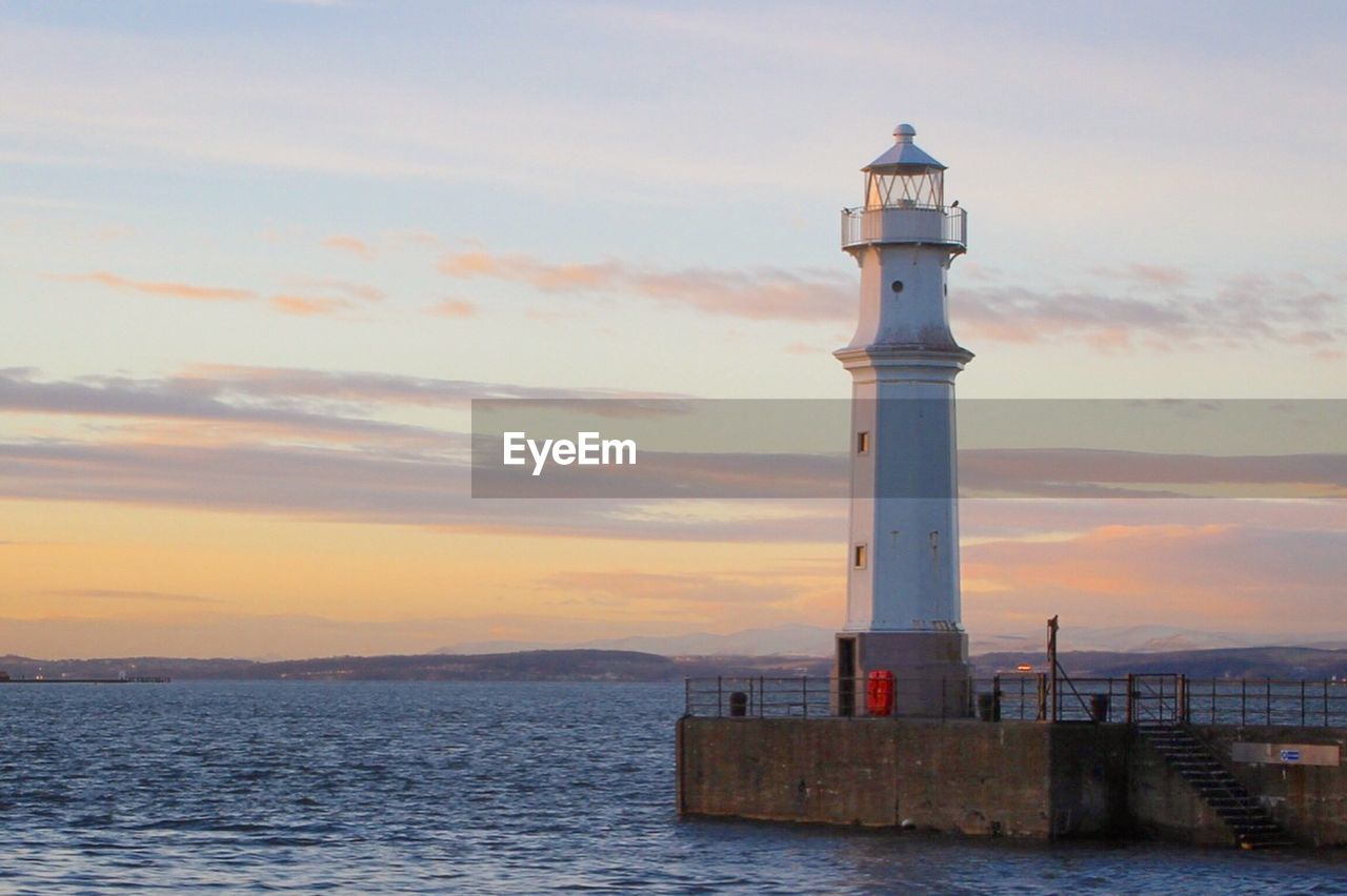 Lighthouse by sea against sky during sunset