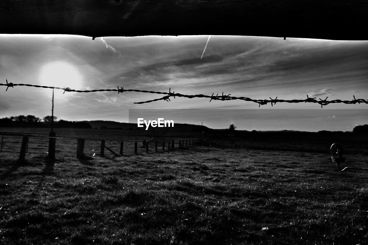 SILHOUETTE OF BARBED WIRE FENCE ON FIELD