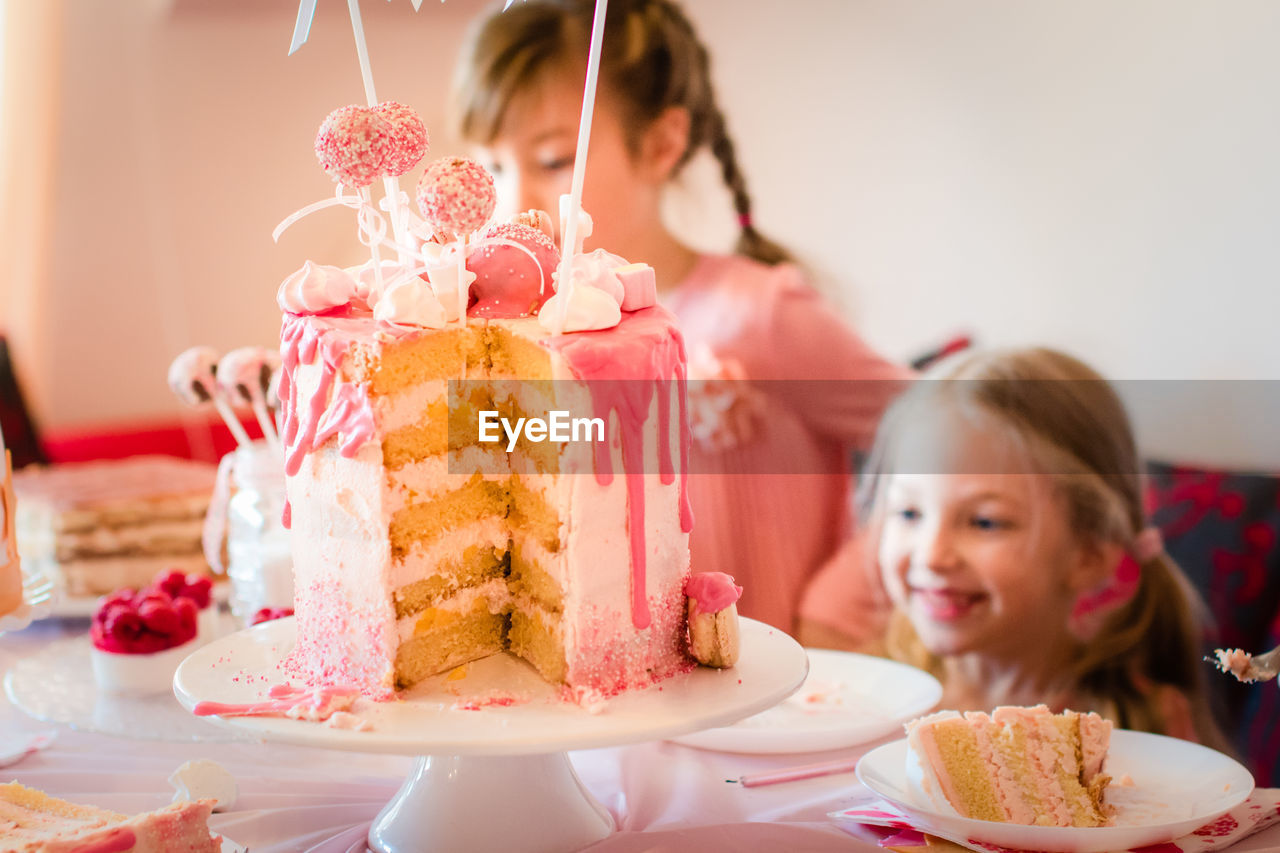 Close-up of birthday cake on decorated table with siblings in background