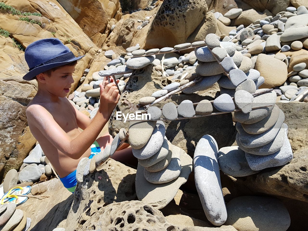 Shirtless boy on stacking pebbles at shore during sunny day