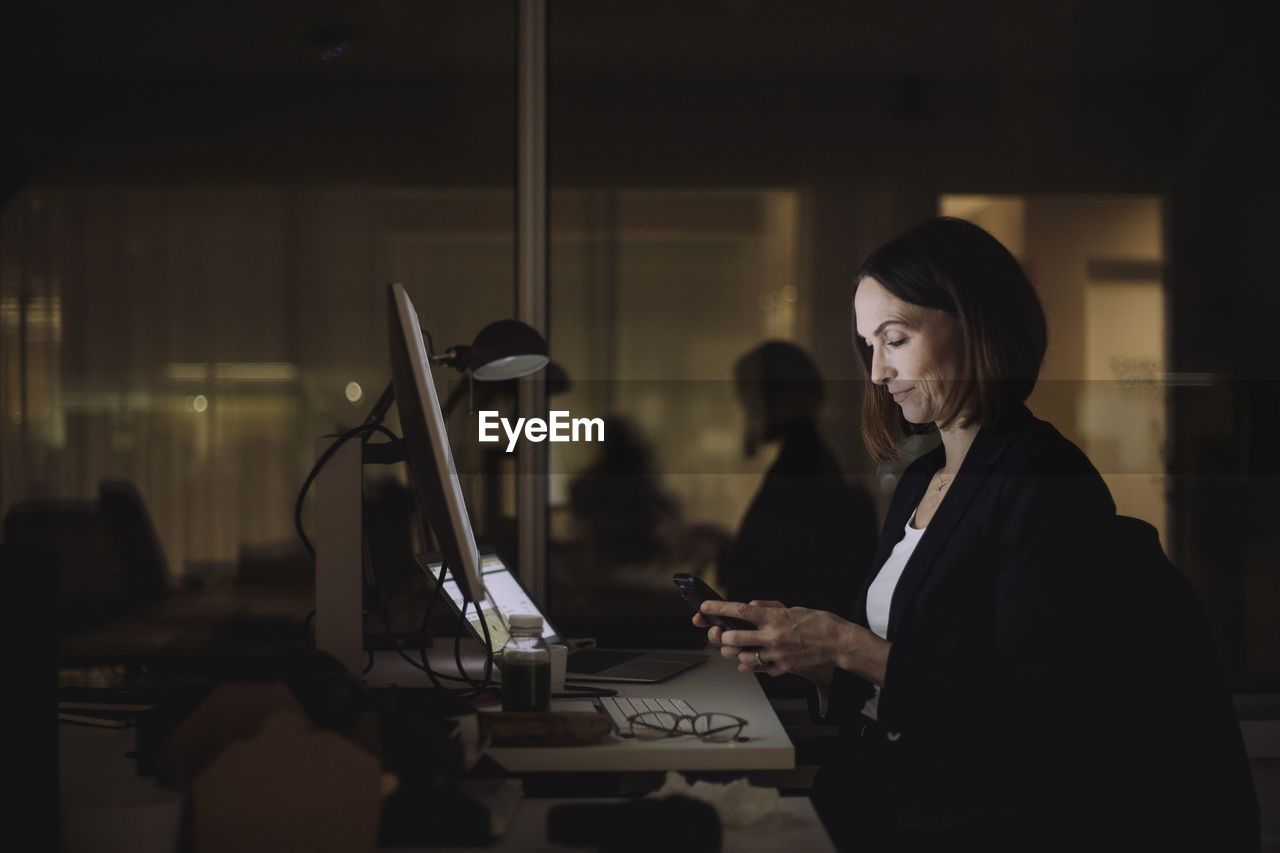 Businesswoman using smart phone while working overtime at work place