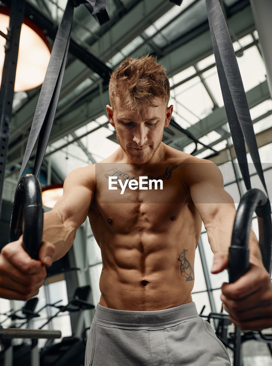 portrait of shirtless young man exercising in gym