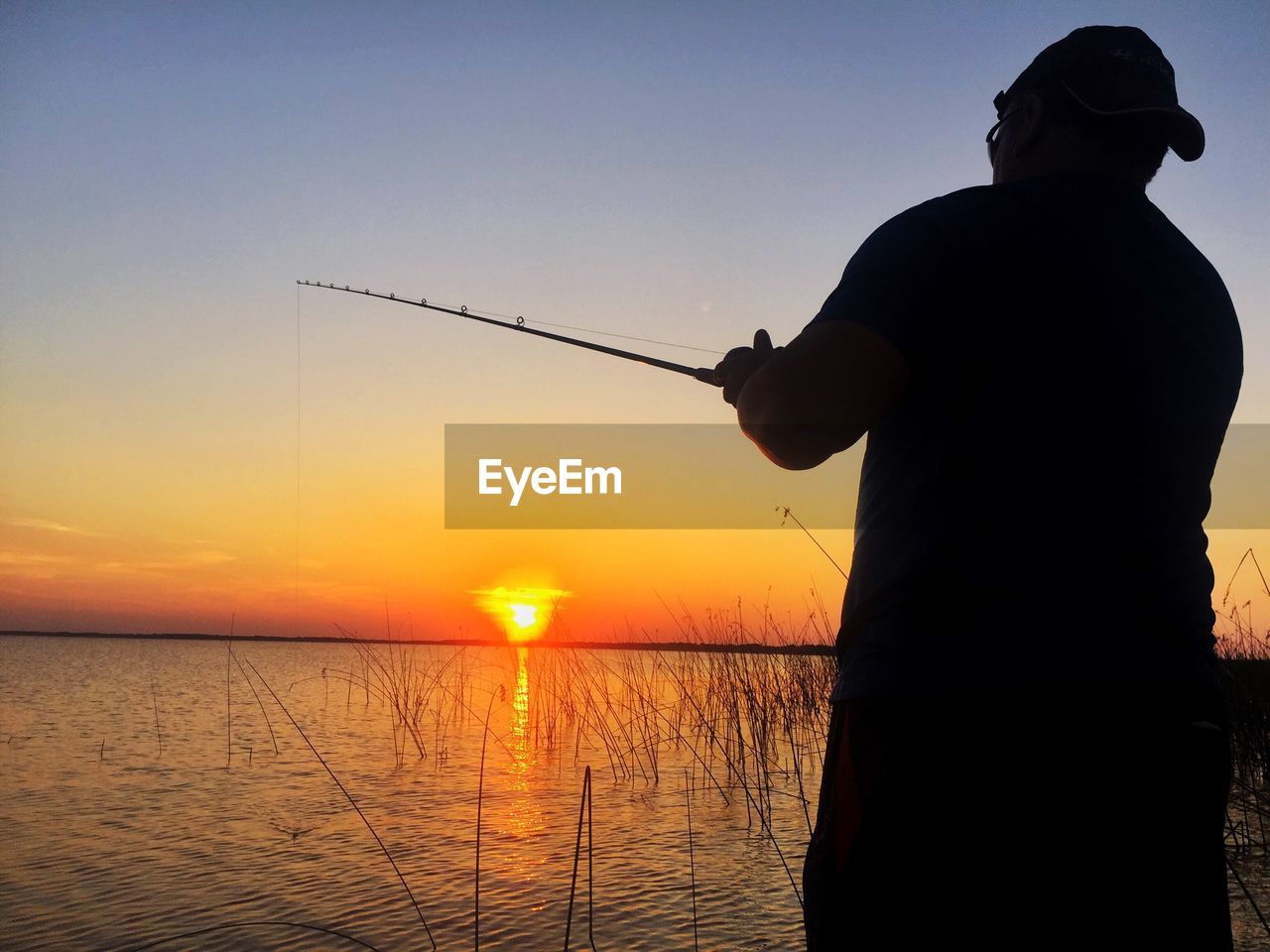 Rear view of silhouette man fishing in sea against clear sky during sunset