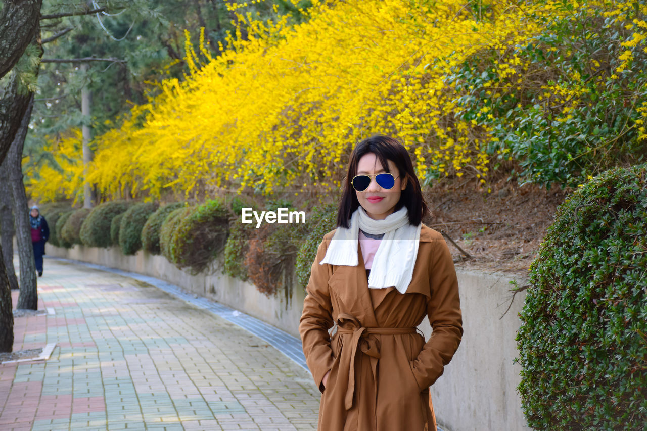 Portrait of fashionable woman standing on footpath against plants