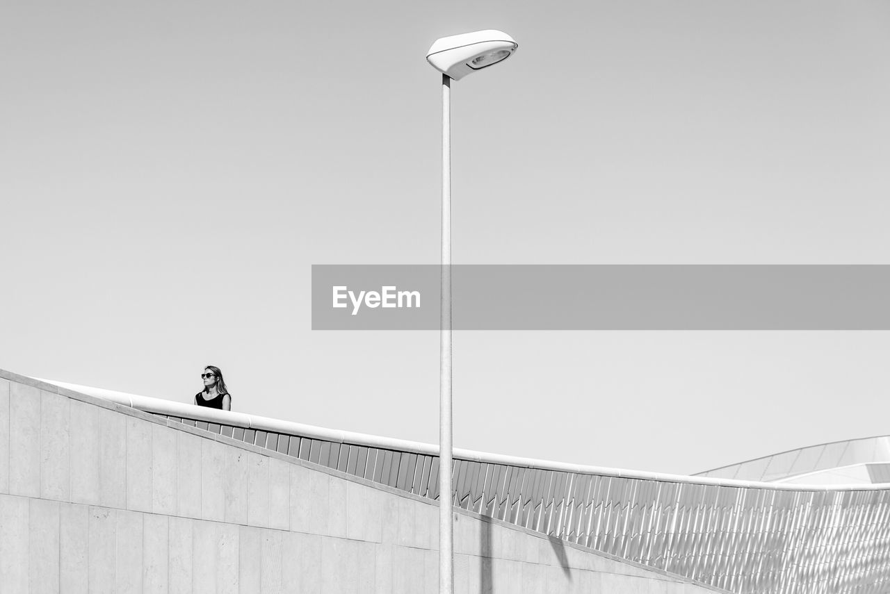 LOW ANGLE VIEW OF WOMAN ON STREET LIGHT AGAINST CLEAR SKY