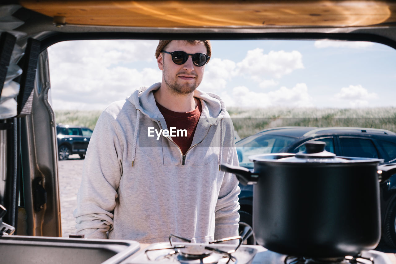 Portrait of young man wearing sunglasses standing by car outdoors