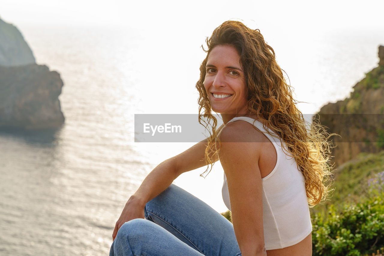 Portrait of smiling young woman sitting against sea