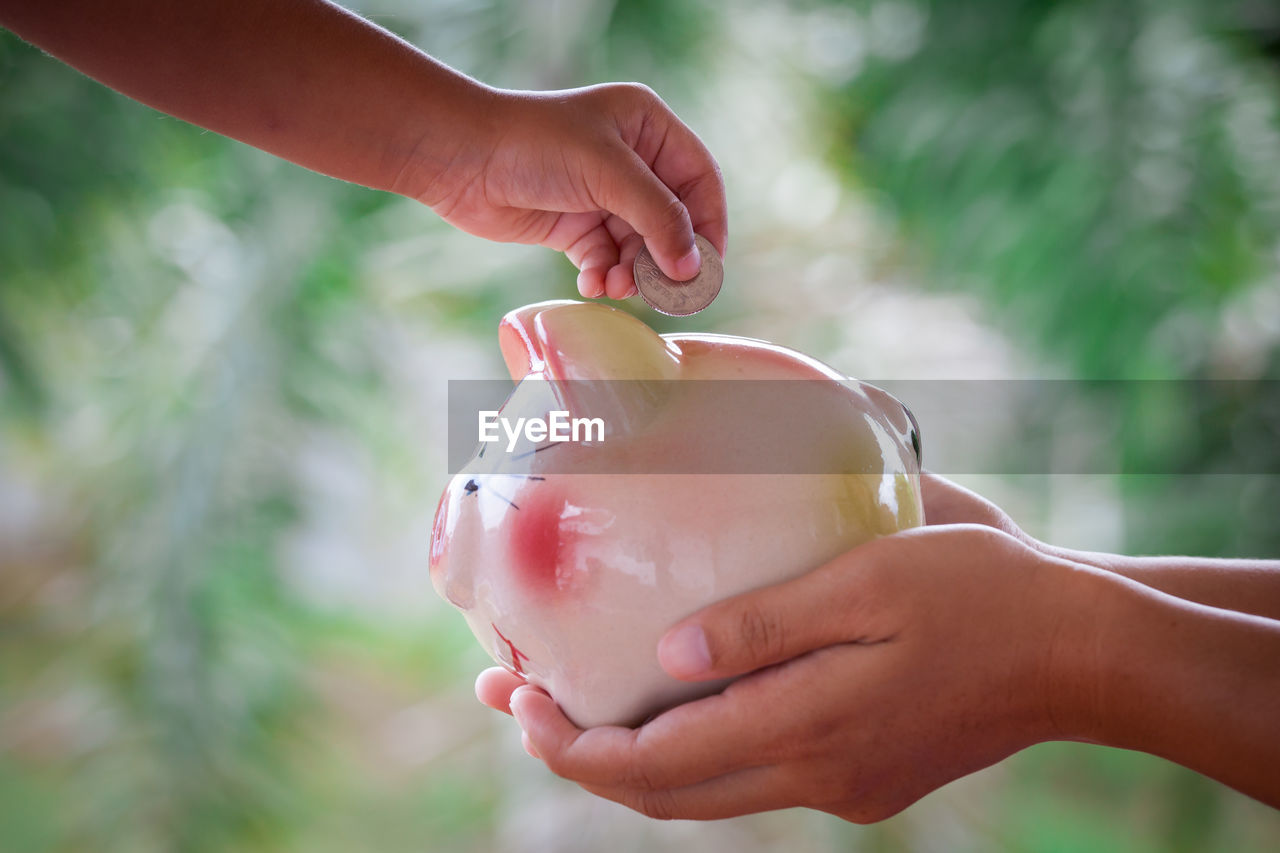 Cropped image of kid putting coin in piggy bank held by mother