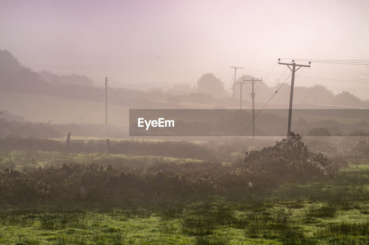 ELECTRICITY PYLON ON FIELD AGAINST SKY