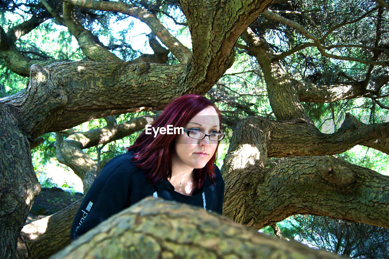 Thoughtful young woman with dyed hair by tree branches