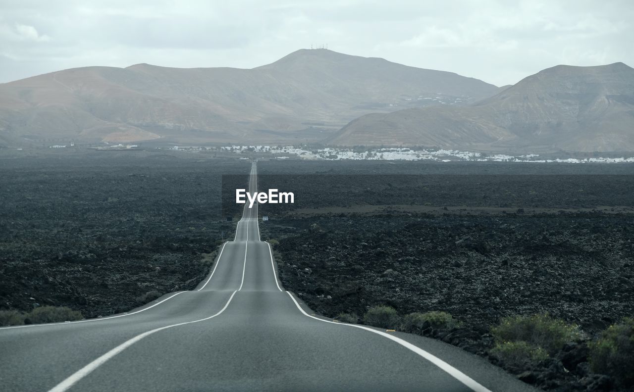 Road leading towards mountains against sky